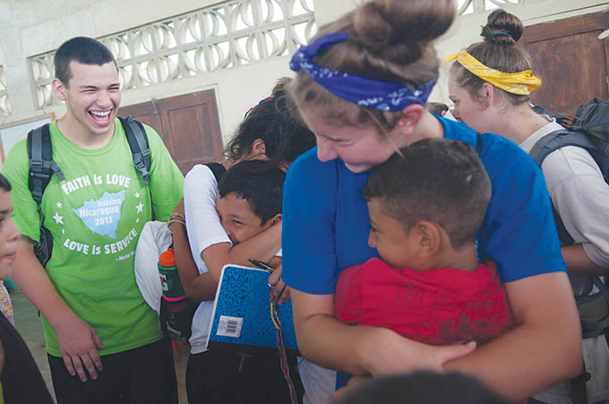 David Murtaugh, from left, Daniela Cruz and Gretchen Theis hug local neighborhood children goodbye as they prepare to load the bus back to Managua after the 10-day long mission trip in Muelle de los Bueyes in Nicaragua.(Jenna Teter/Texas Catholic)