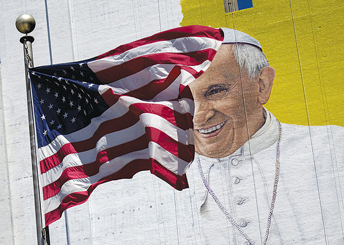 The U.S. flag flies in front of a mural of Pope Francis in New York City, August 28. Pope Francis' 10th foreign trip will be the longest of his pontificate and, with stops in Cuba, three U.S. cities and the United Nations, it also will be a "very complex trip," the papal spokesman said. (CNS photo/Brendan McDermid, Reuters)