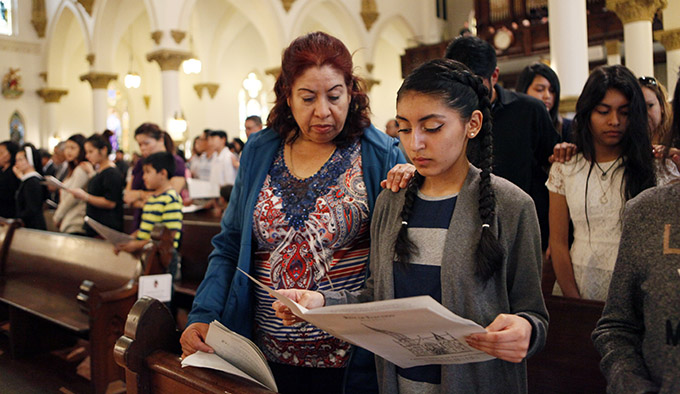 Godmother Eloina Mijares, left, places her arm on the shoulder of Catechumen candidate Melanie Munoz as Bishop Kevin J. Farrell affirms the candidates during the Rite of Election on Feb. 20 at the Cathedral Shrine of the Virgin of Guadalupe in Downtown Dallas. (BEN TORRES/Special Contributor)