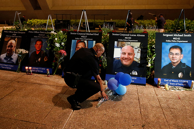 A Dallas police officer picks up balloons and flowers July 11 in front of images of the five slain officers after a candlelight vigil at Dallas City Hall. A gunman shot and killed five police officers and wounded seven during a peaceful protest July 7 in downtown Dallas. (CNS photo/Carlo Allegri, Reuters)