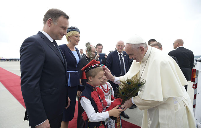 Pope Francis receives a gift from a child as he is greeted by Polish President Andrzej Duda and first lady Agata Kornhauser-Duda upon his arrival at the airport in Krakow, Poland, July 27. (CNS photo/L'Osservatore Romano via EPA)