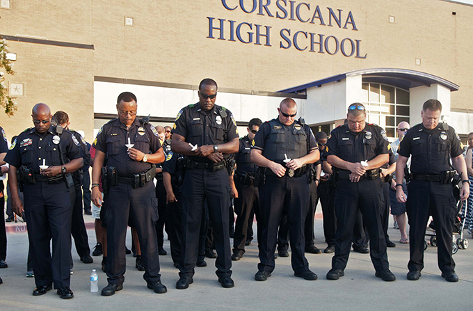Dallas Area Rapid Transit officers bow their heads in prayer during a candlelight vigil for DART Police Officer Brent Thompson at Corsicana High School on July 10. (JENNA TETER/The Texas Catholic)