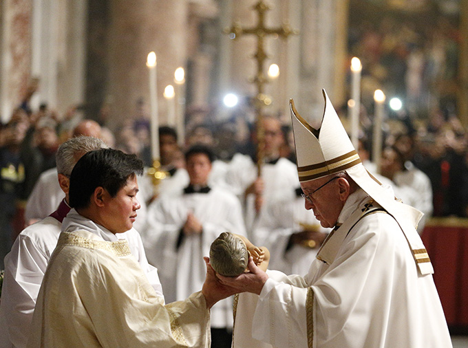 Pope Francis presents a figurine of the baby Jesus to an altar server at the conclusion of Christmas Eve Mass in Peter's Basilica at the Vatican Dec. 24. (CNS photo/Paul Haring)
